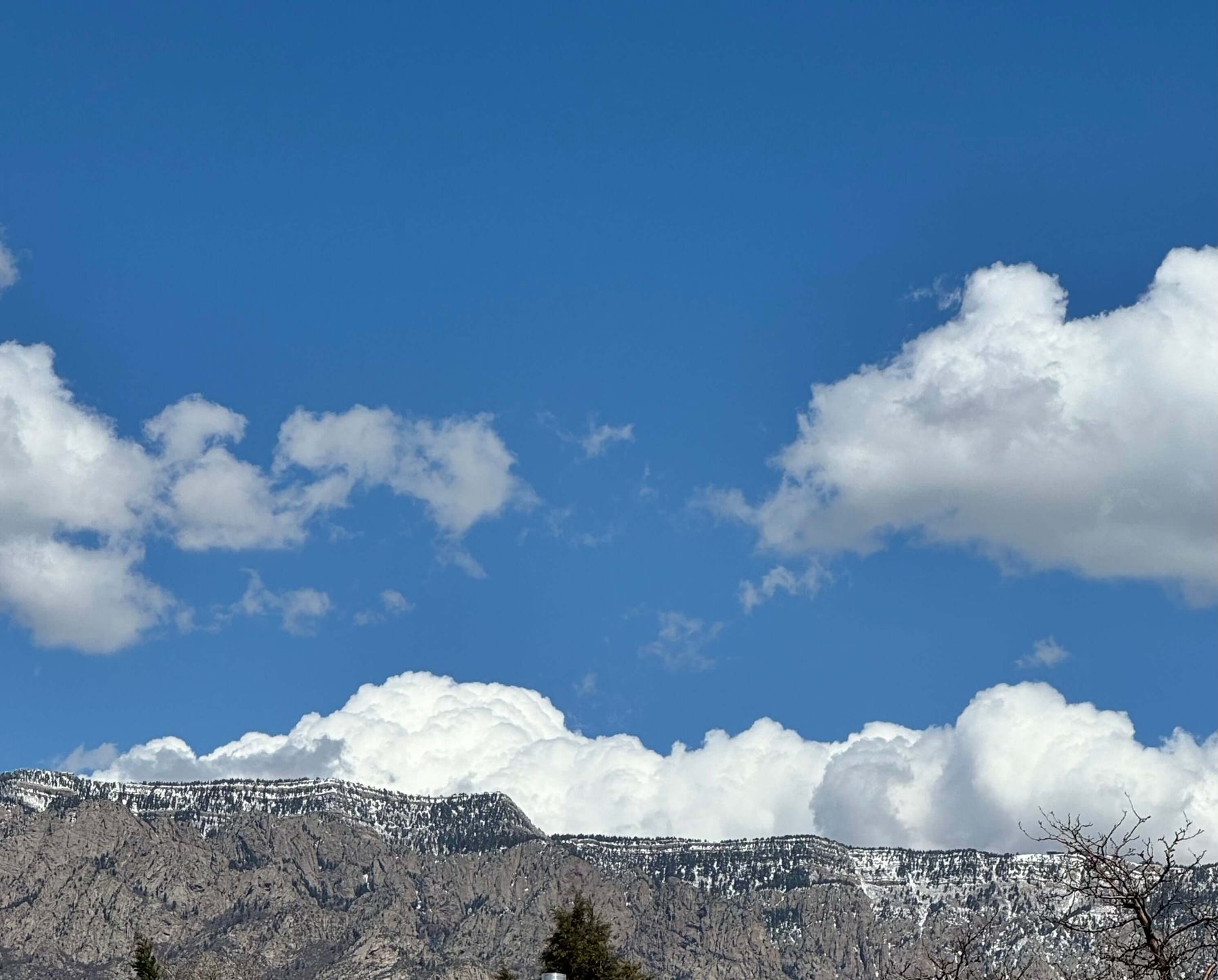 Majestic mountain range under a clear blue sky with fluffy white clouds, symbolizing reaching new heights with positive self-talk.