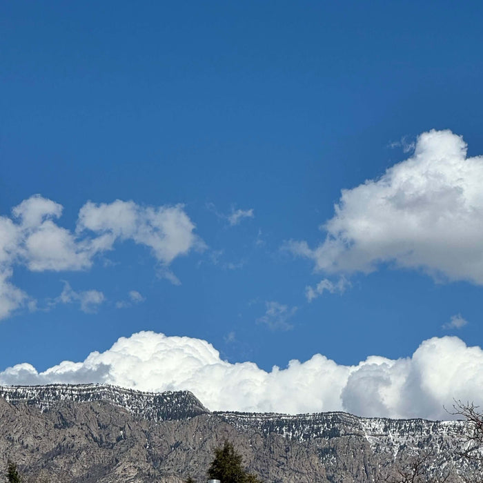 Majestic mountain range under a clear blue sky with fluffy white clouds, symbolizing reaching new heights with positive self-talk.