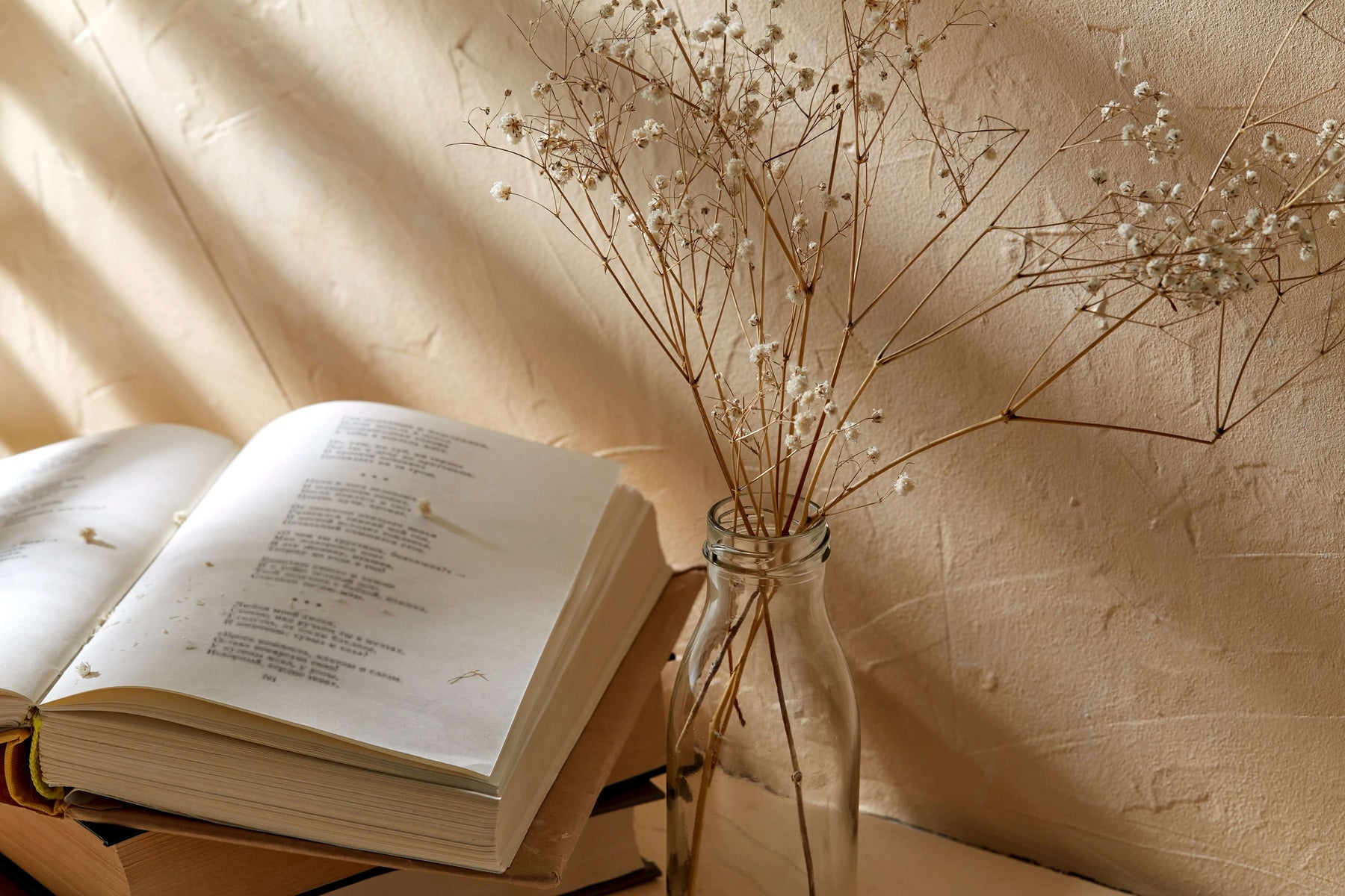 Open book and vase with dried flowers on a textured surface with soft lighting.