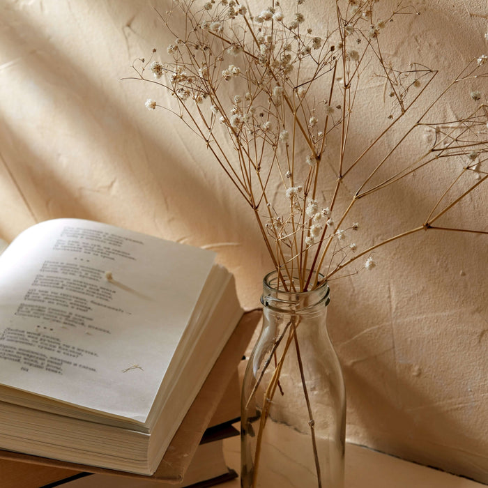 Open book and vase with dried flowers on a textured surface with soft lighting.