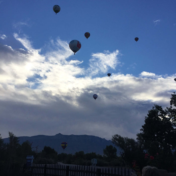 Hot air balloons floating against a vibrant blue sky with scattered clouds and distant mountains.