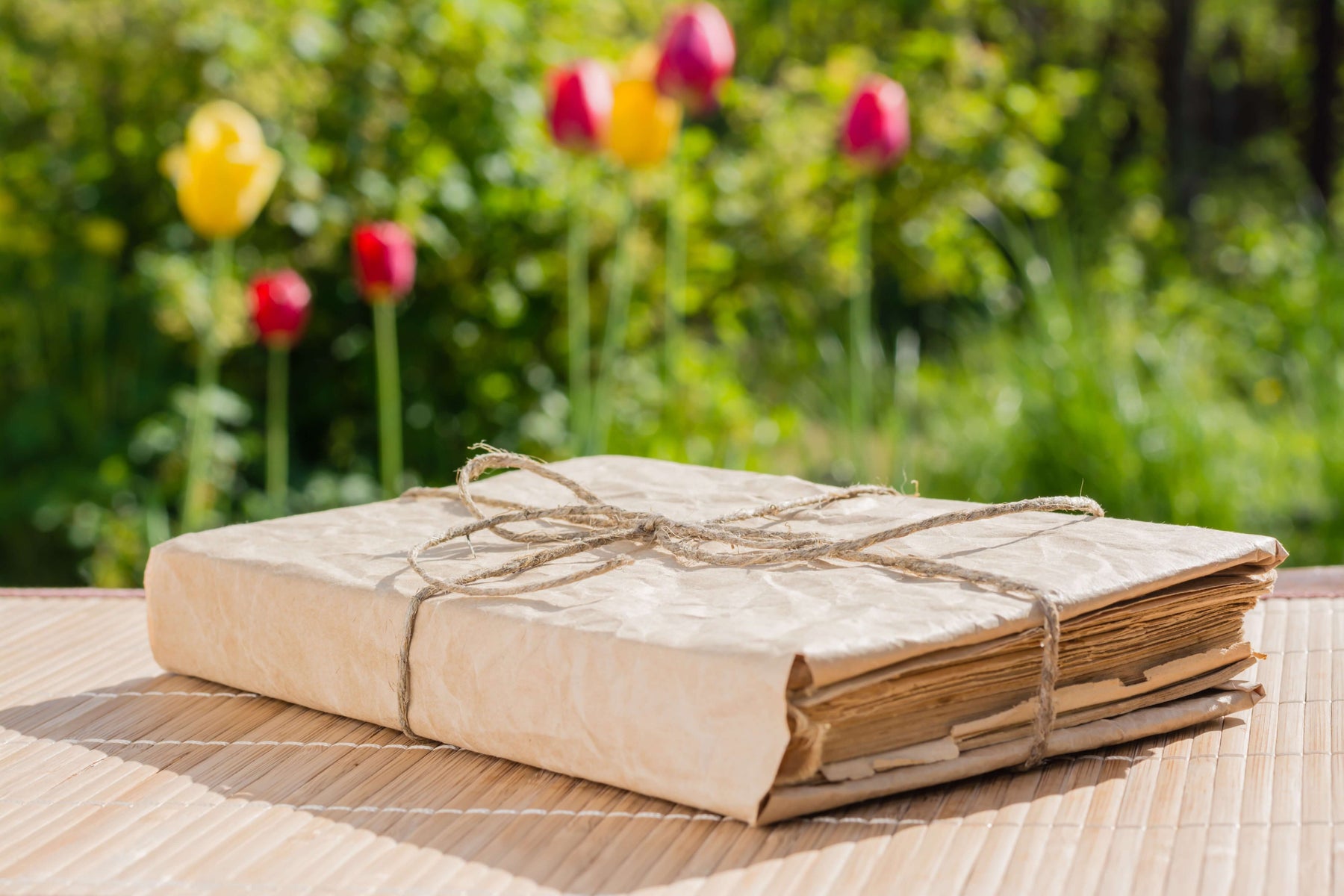 Vintage book wrapped in twine on bamboo mat with colorful tulips in background